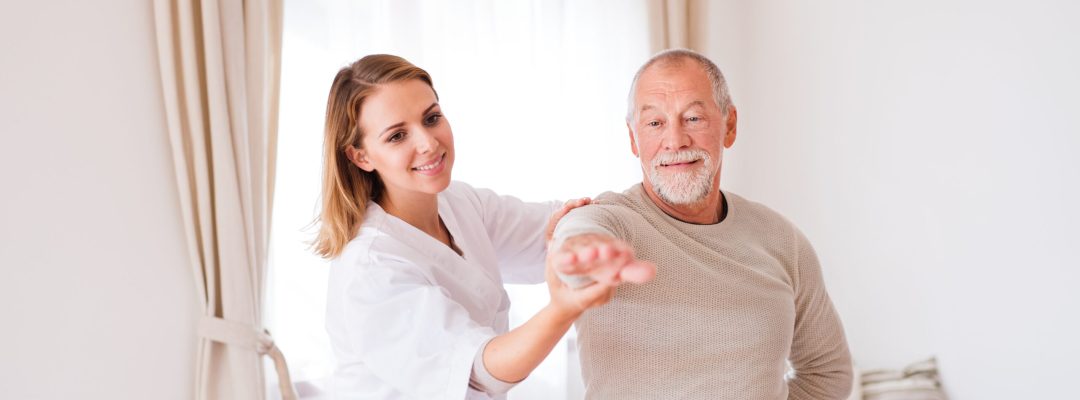 Health visitor and a senior man during home visit. A nurse or a physiotherapist helping a senior man exercise.